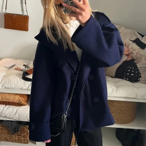 Mörkblå kappa med knappar - Snygg mörkblå kappa med stora knappar och bred krage. Perfekt för kyligare dagar. Den har en elegant och tidlös design som passar till många olika stilar. Köpt på Designbysi för 700kr, knappt använd (som ny)