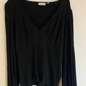 Svart ribbad topp från Kappahl - Snygg svart ribbad topp från Kappahl med v-ringad design. Toppen har långa ärmar och en stilren look som passar perfekt till olika tillfällen. 