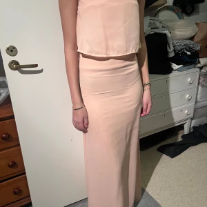 Ljusrosa långklänning med detaljer - Elegant ljusrosa långklänning med en ärmlös design och glittriga detaljer längs ryggen. Perfekt för speciella tillfällen med sin stilrena och sofistikerade look.Perfekt för bal och liknande 