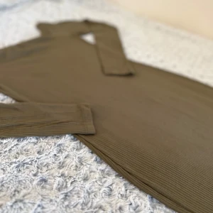 Olivgrön ribbad klänning från NA-KD - Snygg olivgrön klänning från NA-KD i ribbat material. Den har en figurnära passform och långa ärmar, perfekt för både vardag och fest. Klänningen är knälång och har en stilren design som passar till många tillfällen. Skicken är i perfekt form, använd 1-2 gånger som max!