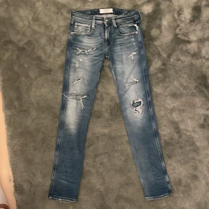 Replay jeans med slitningar. Anbasss, slim fit - Snygga blå jeans med slitningar och en cool, tvättad look. De har en klassisk femficksdesign och en dragkedja. Perfekta för en avslappnad stil.. modellen är anbass slim fit 