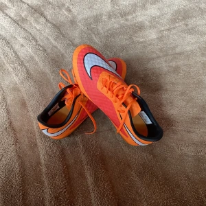 Nike fotbollsskor(hypervenom)  - Snygga orange fotbollsskor från Nike med svarta och vita detaljer. Skorna har snörning och en slitstark sula med dobbar för bra grepp på planen. Perfekta för fotbollsspelare som vill sticka ut på planen. Otroliga hypervenom. För mer info, hör av er. Först till kvarn!
