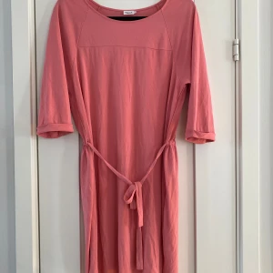 Rosa klänning från Filippa K - Säljer en söt rosa klänning från Filippa Kmed trekvartsärmar och knytband i midjan. Perfekt för en avslappnad stil. Klänningen har en enkel design och är gjord i ett mjukt material. Ny ljusrosa klänning i strl S från Filippa K, modell crepe tonic dress.  Ny, aldrig använd.  Mått Över bröstet: ca 55 cm Längd från axeln och ner: ca 90 cm  80% acetate och 20% polyamid   Kommer från ett djur och rökfritt hem.