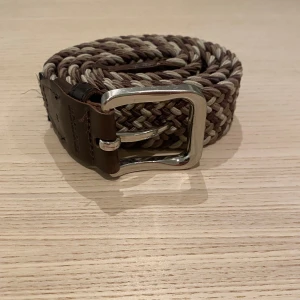 Flätat bälte från Jack & Jones - Snyggt flätat bälte från Jack & Jones i bruna och beige toner. Bältet har en robust silverfärgad spänne och detaljer i brunt skinn. Perfekt för att ge en stilren touch till din outfit. Aldrig använt innan och inga tecken på användning. Pris kan diskuteras vid snabb affär