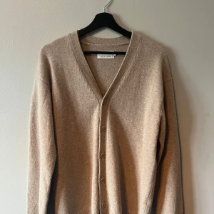 Beige kofta från Casual Friday - Säljer en stilren beige kofta från Casual Friday. Koftan har en v-ringad design med knappar framtill och långa ärmar. Perfekt för en avslappnad och snygg look. 🧥