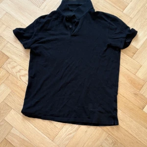 Svart kortärmad pikétröja - Säljer en  svart pikétröja med korta ärmar och knappar vid kragen. 