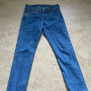 Blå Levis 501 jeans - Klassiska blå Levis 501 jeans med en straight passform. De har en knappgylf och femficksdesign. Perfekta för en tidlös stil. Pris kan absolut alltid diskuteras