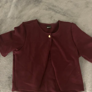 Vinröd kortärmad kofta - Snygg vinröd kofta från Gina Tricot med en enkel knapp framtill. Perfekt för att ge en stilren touch till din outfit. Den har en elegant design med trekvartsärmar.