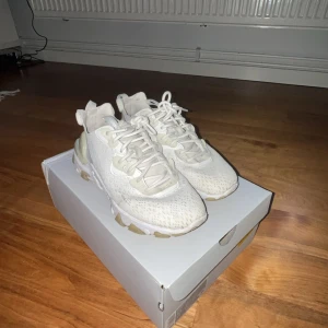 Vita Nike react  - Säljer ett par stilrena vita sneakers med snörning. Skorna har en modern design med en bekväm sula och detaljer i syntetmaterial. Perfekta för en avslappnad look. Skorna är använda men fortfarande ett bra skick.