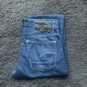 G-star jeans  - Snygga blå G-star jeans med klassisk design och fem fickor. De har en knappgylf och en stilren bakficka med dekorativ söm. Perfekta för en avslappnad look.