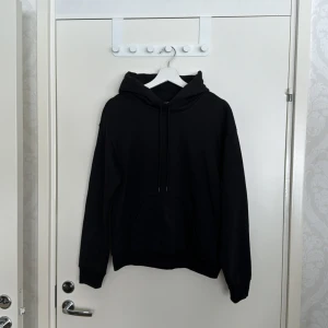 Svart hoodie från H&M - Säljer en stilren svart hoodie från H&M i storlek XS. Den har en avslappnad passform med en klassisk känguruficka och justerbar huva. Perfekt för en casual look. Inga defekter. 