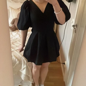 Svart klänning med puffärmar - Snygg svart klänning med puffiga kortärmar och v-ringning. Den har en knytning i ryggen som ger en fin detalj. Perfekt för en stilren look.