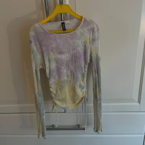 Flerfärgad ribbad topp  - Säljer en snygg flerfärgad ribbad topp. Toppen har långa ärmar och en unik knytning framtill som ger en fin detalj. Perfekt för att liva upp garderoben med lite färg!