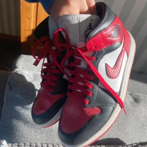 Nike Air Jordans i rött, svart och vitt - Säljer ett par klassiska Nike Air Jordans i en snygg färgkombination av rött, svart och vitt. Skorna har den ikoniska Air Jordan-loggan på sidan och är utrustade med snörning för en perfekt passform.