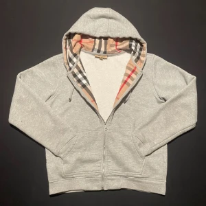 Grå burberry hoodie - Säljer en stilren grå hoodie från Burberry med dragkedja och klassiskt rutigt mönster i huvan✨. Perfekt för en avslappnad look😁