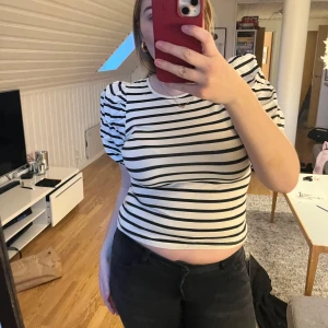 Randig kortärmad topp - Säljer en randig topp med puffiga korta ärmar. Den är svart och vit med ett klassiskt randigt mönster. Toppen är croppad och har en tight passform, perfekt för en stilren look.