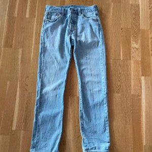 Levi's 501 ljusblå jeans - Klassiska Levi's 501 jeans i en snygg ljusblå färg. De har en rak passform och är tillverkade i slitstarkt denim. Perfekta för en avslappnad stil med den ikoniska Levi's-lappen på baksidan. Perfekt till sommar outfiten 