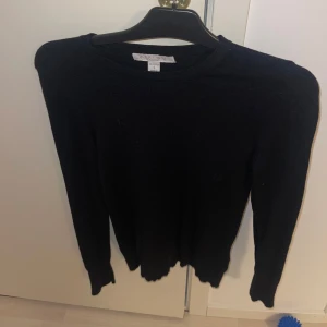 Svart tröja med knappar - Snygg svart tröja med långa ärmar och dekorativa knappar vid ärmsluten. Perfekt för en stilren look.