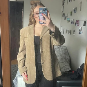 Beige manchesterkavaj - Snygg beige kavaj i manchester med knappar framtill. Perfekt för en stilren look. Funkar både som kavaj och jacka och har inge täcken på användning. I plagget är storleken ”C100” vilket är mellan M/L. Extra knappar finns i innerfickan 