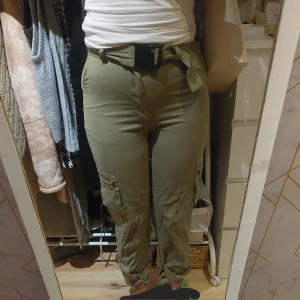Olivgröna cargobyxor med bälte - Snygga olivgröna/militärgröna cargobyxor med hög midja och knytbälte. Byxorna har flera fickor och dragkedjedetaljer på sidorna. Aldrig använda. Passar även XS. Skriv vid frågor eller diskussion av pris! 