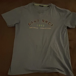 Blå t-shirt från Gant - Säljer en blå t-shirt från Gant med tryck 'GANT NHCT 1949 New Haven Connecticut' på framsidan. T-shirten är kortärmad och har en rund halsringning. Perfekt för en avslappnad stil. Pris kan diskuteras 