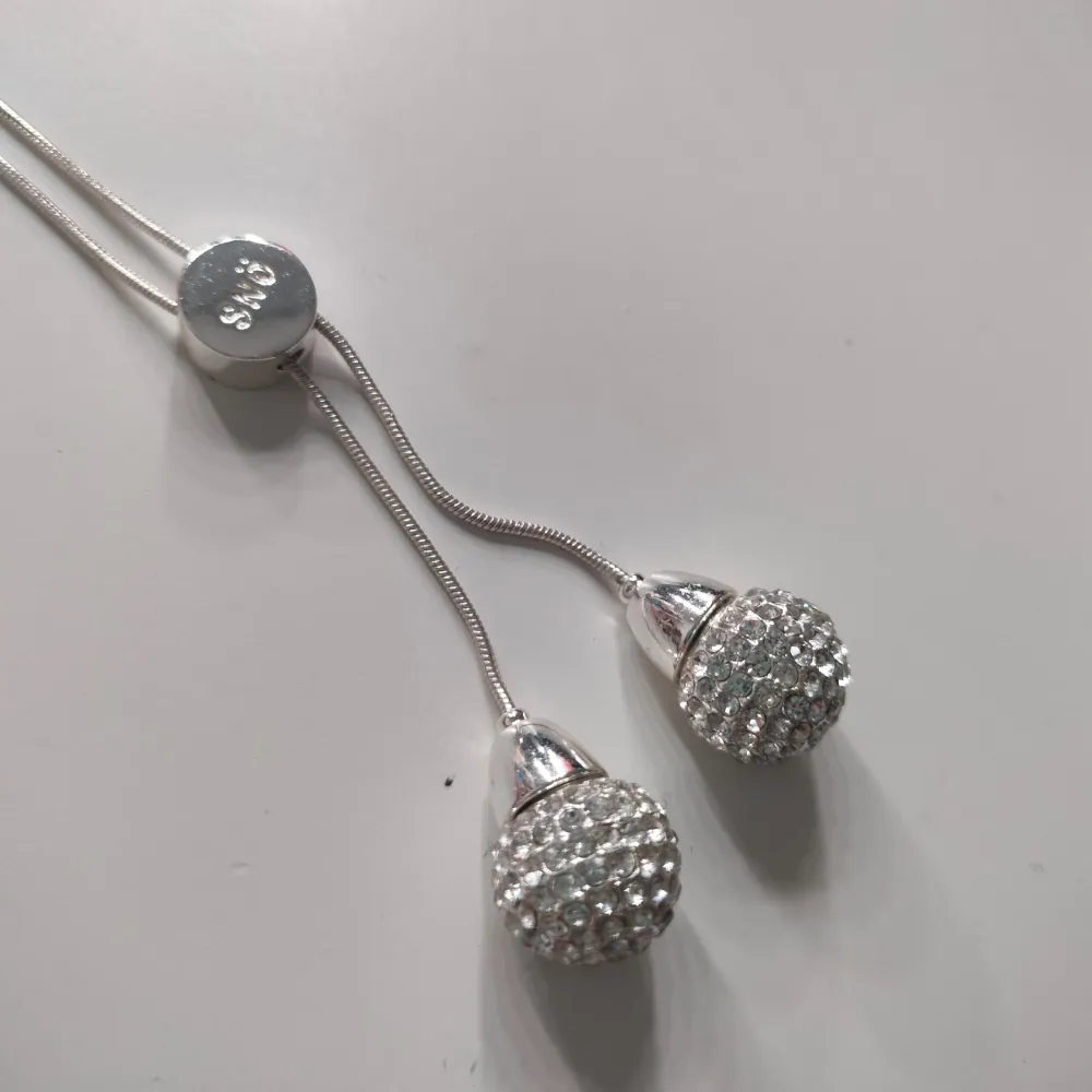 Elegant halsband från SNÖ of Sweden med två glittriga, droppformade hängen. Halsbandet är i silverfärg och har en justerbar längd. Perfekt för att lägga till en touch av glamour till din outfit. Aldrig använt.. Asusteet.