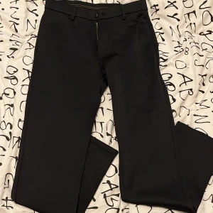 Svarta kostymbyxor - Snygga svarta kostymbyxor med en stilren design. Byxorna har en dragkedja framtill och knappar bak. Tillverkade i en blandning av nylon, viskos, spandex och silke för en bekväm passform.