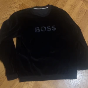 Svart sammetströja från Boss - helt ny Snygg svart sammetströja från Boss med texten 'BOSS' broderad på framsidan. Tröjan har långa ärmar och en rund halsringning. Perfekt för en stilren look. storlek M, lite bättre pris vid snabb affär, skicka för mer bilder
