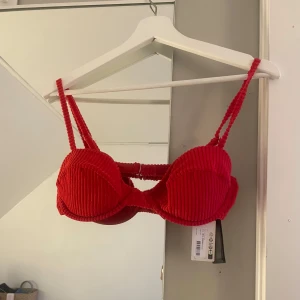 Röd ribbad bikini från NA-KD - Snygg röd bikini från NA-KD med ribbad textur. Överdelen har vadderade kupor och justerbara axelband för perfekt passform. Underdelen är i en klassisk modell som matchar toppen. Storleken i överdelen är 80C och underdelen är storlek M
