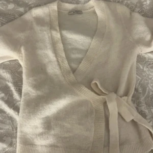 Omlott cardigan - Säljer en stilren vit omlottkofta med knytband i midjan. Inte kommit till användning då den är för liten. I nyskick
