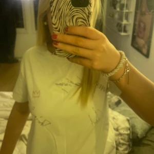 Vit t-shirt med tryck - Säljer en vit hov1 t-shirt med tryck och autografer på framsidan. Baksidan har ett stort tryck med texten 'AROUND THE WORLD TOUR' och en lista över de olika städer och datum de spelade på den sommaren. Alla Hov1s medlemmar har skrivit sitt namn på den!