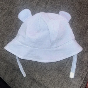 Ljusblå hatt med öron - Söt ljusblå hatt med små öron på toppen. Perfekt för att ge en lekfull touch till din outfit. Hatten har knytband för att hålla den på plats.