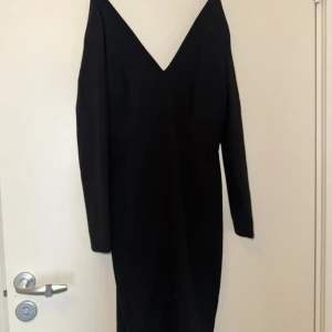 Svart långärmad klänning med v-ringning - Elegant svart klänning med lång ärm och djup v-ringning. Perfekt för en stilren look. Klänningen har en figurnära passform och är tillverkad i ett mjukt material.