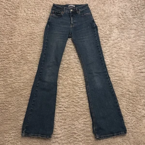Blå bootcut jeans från Gina tricot  - Snygga blå bootcut jeans från Gina tricot. De har en klassisk femficksdesign och en knappgylf. Perfekta för en avslappnad stil med en touch av retro.