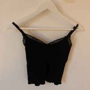 Linne med spets - Svart topp med spetsdetaljer och justerbara band från Urban Outfitters. Stl S, men skulle mer säga en liten XS.