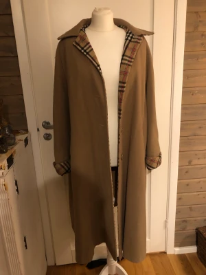 Kappa i ull. - Skön kappa med ”burberry-linjering” (obs inte äkta burberry). Fint skick. Finns ingen storlek på den men skulle passa S-L beroende på hur man vill att den ska sitta.