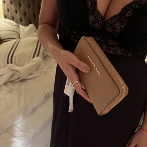 Michael kors plånbok  - En helt oänvänd Michael Kors plånbok med Tag kvar. Kan hämtas i Stockholm C (även postas) Elegant och trendig och kan användas som både handväska och plånbok. Alla original tags och kort finns kvar i plånboken.