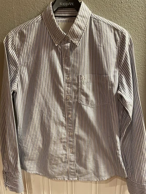 Randig damskjorta - 100%bomull Använd en gång  Button down krage 7knappar fram, extraknappar finns  Bröstficka  Lite figursvängd  Storlek M Längd 66 cm Bystmått tvärs över 49 cm   