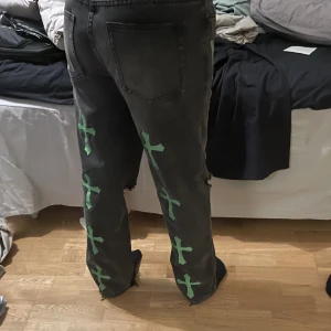 Svarta jeans med tryck - Svarta jeans med gröna kors tryck på baksidan och tryck i samma stil där fram. I ett bra skick!
