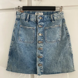 Jeanskjol  - Snygg, kort jeanskjol med knappar längst framsidan och fickor både fram och bak. 