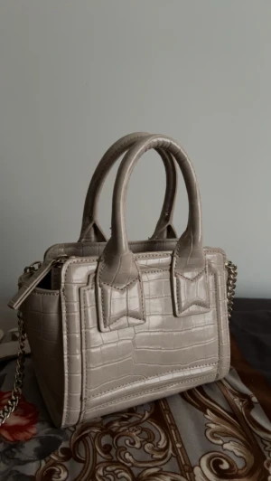 Väska - Detta är en väska som jag köpt för inte så längesen knappt använd, den är beige o om du vill kan du ta bort banden från väskan, du bestämmer själv. 