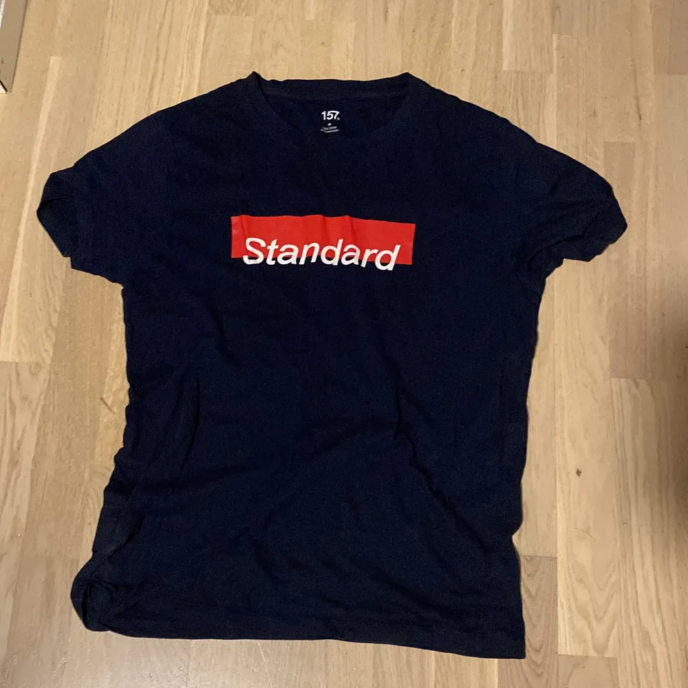 Mörkblå t shirt med texten ”standard”. T-shirts.