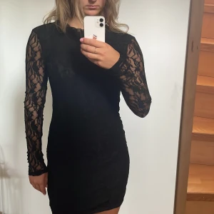 svart spetskkännibg - Kort, långarmad, tajt klänning.  Helt tävkt av spets. Dragkedja i ryggen. Vila st. S