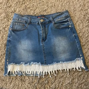 Jeanskjol - Söt jeanskjol med lite spets/fransar längst ned! Och två rhinestones på varsin sida. Skriv för mer bilder eller bilder på! Står storlek 44 men jag har 34 och den passar jättebra.