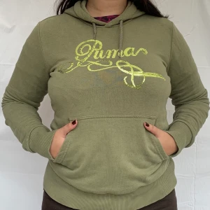 Grön puma hoodie - Grön puma hoodie med logga över bröstet i paljetter, alla är kvar. Den har även en ficka på magen och liten pumalogga på ena ärmen (se sista bilden). Mycket bra skick.
