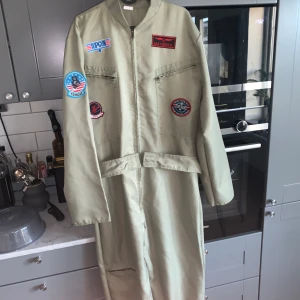 Top Gun Dräkt, Pilot - Är 1,86 m och den passar Ganska lång i armar och ben men går att vika upp utan problem Har flera fickor som fungerar och alla dragkedjor fungerar som de ska. Dräkter är endast använd en gång förra halloween  Nypris från Buttericks- 950kr