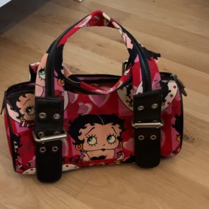 väska med Betty Boop på - En as snygg växa med Betty Bop på! Det finns två innerfack och ett fack med dragkedja inuti! Säljer för 130kr, kan mötas upp i sthlm 💘