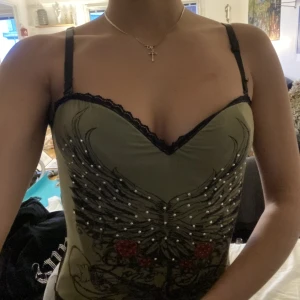 Topp med ängeltryck av strass - Topp med tryck av strass och ängelvingar. Superfin. Formad som korsett men sitter inte som en korsett (man kan andas). Inga fläckar eller hål. Skriv vid funderingar!