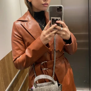 Läderimitation kappa - En brun röd kappa från nakd med knytning runt midjan  Köparen står för frakten