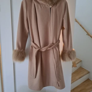 Kappa  - Superfin kappa. Strl 40 (M) Nypris: 1500kr Lyxig kappa med pälsdetaljer från CHAIRA FORTHI. - Kappan har pälsdetaljer runt ärmöppning och huva. - Dekorativt band i midjan - Två fickor framtill - Stum vävd kvalité Mått i storlek small: totallängd från axel